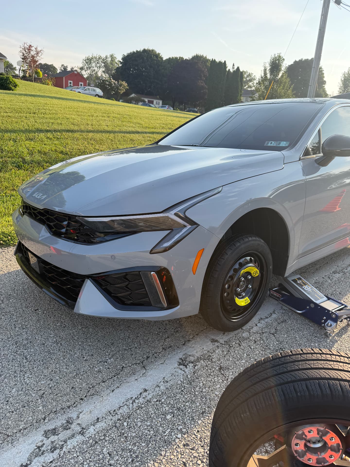 Kia K5 raised on a floor jack during a roadside tire change