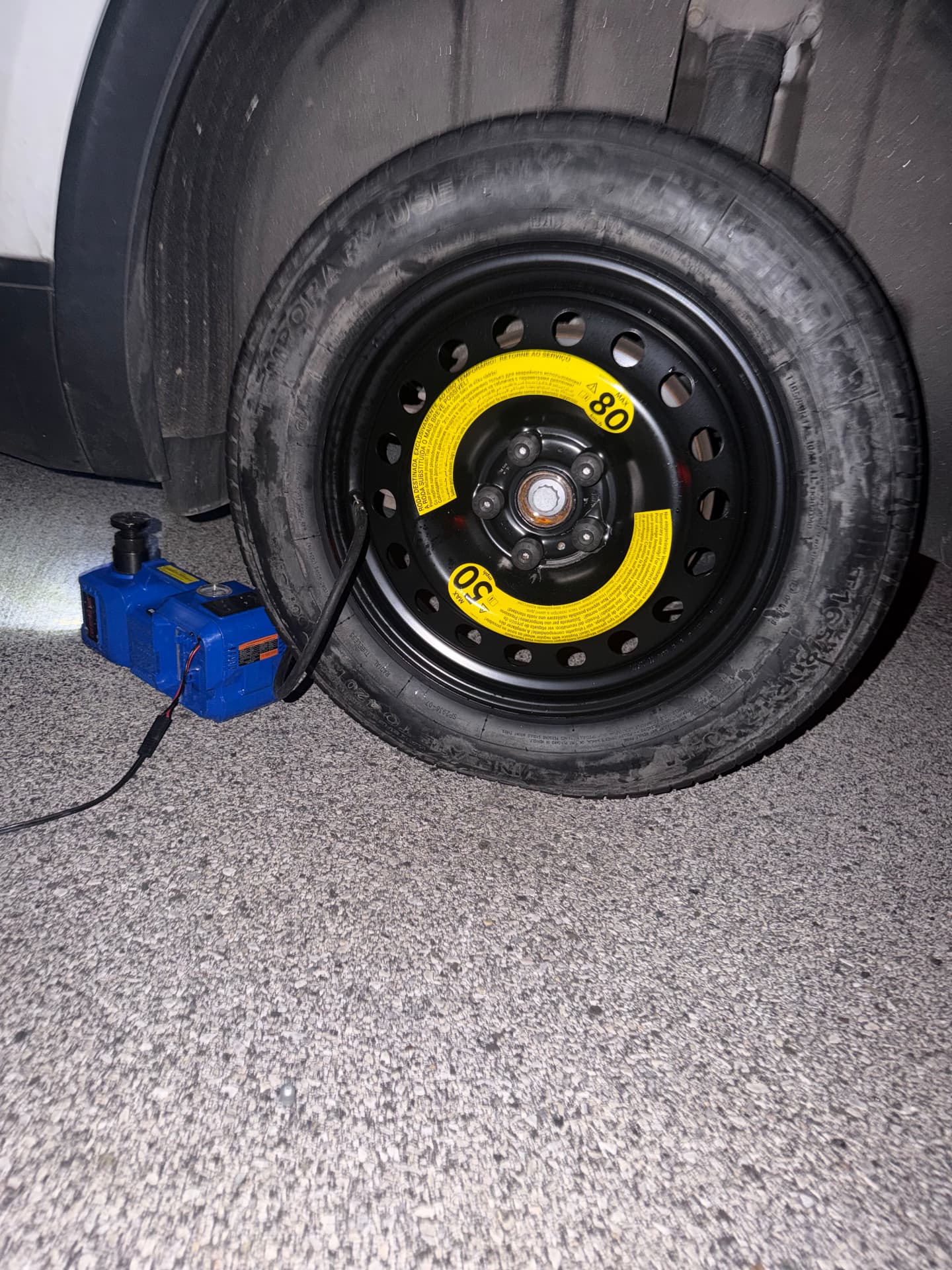 Compact spare tire inflated with a portable jack at night